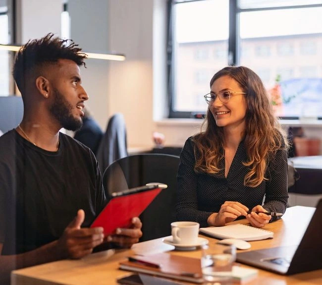 Two coworkers, talking at a table