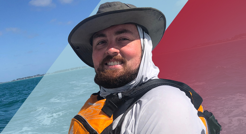 Photo of Kyle in a sail boat, with the sea in the background.