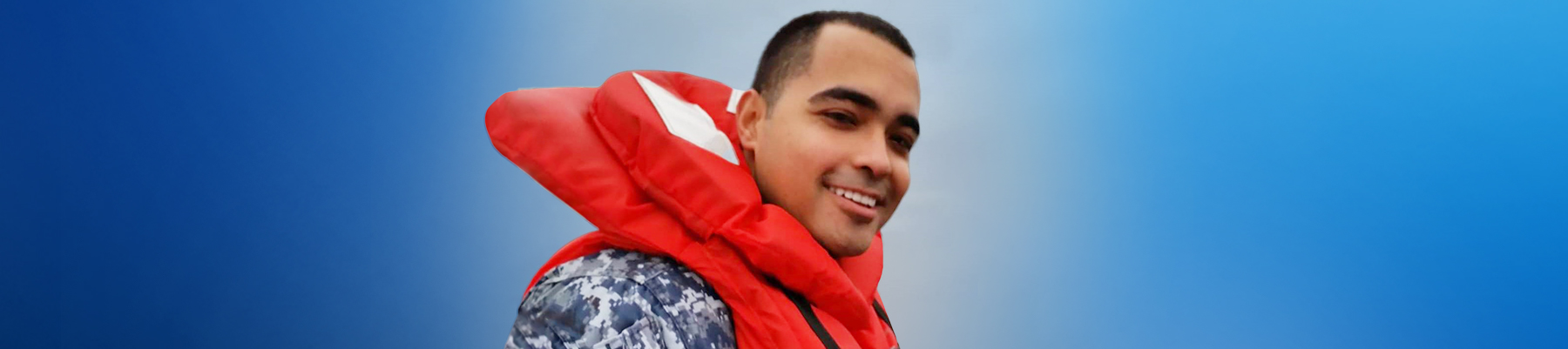 Photo of Alex wearing a military uniform and life vest, looking to the camera smiling.