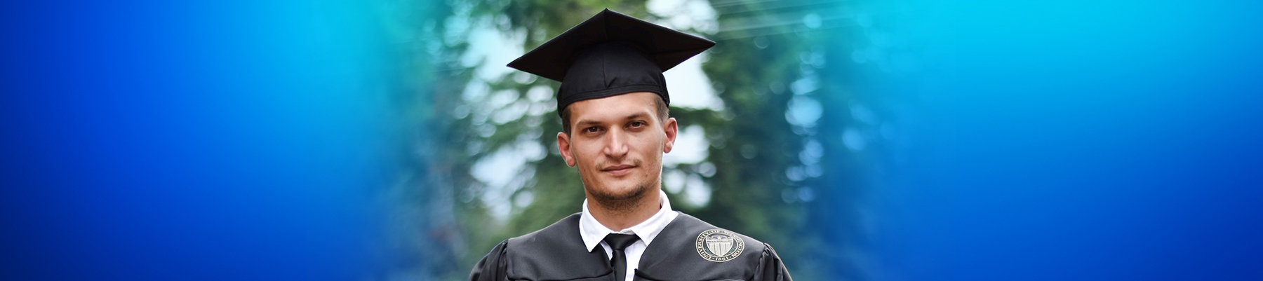Photo of Vadym wearing his graduate gown, facing the camera and smiling 