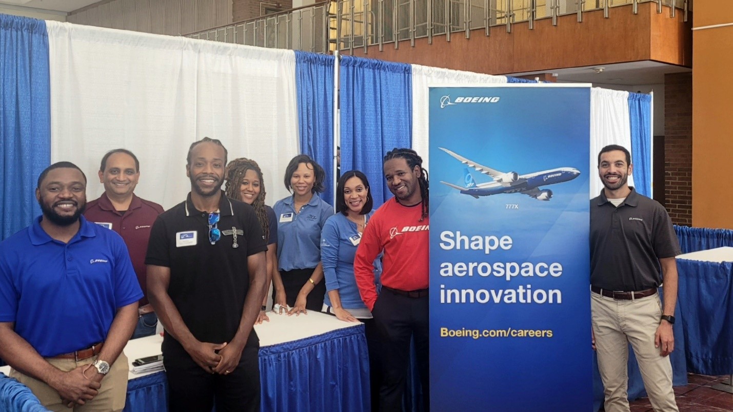 Anika poses with a group of students near a Boeing booth at a careers fair. 