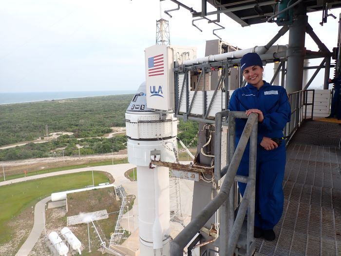 Melanie is standing on a platform with the Starliner visible in the background. 