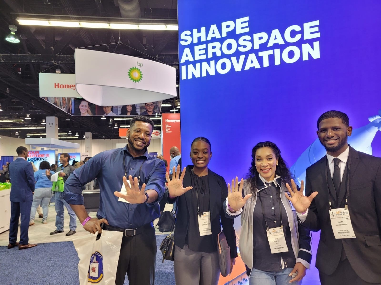 Anika poses in front of a "Shape Aerospace Innovation" banner with teammates, holding palms up to signify region five