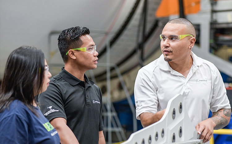 two engineers wearing safety goggles and chatting in front of a large aerospace project