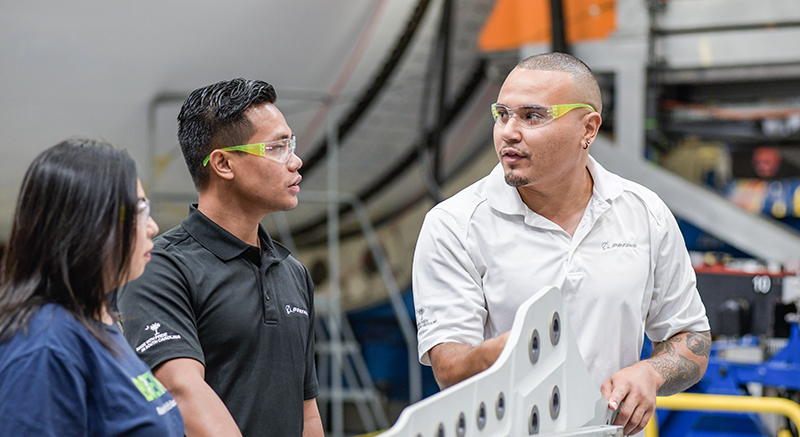 two engineers wearing safety goggles and chatting in front of a large aerospace project