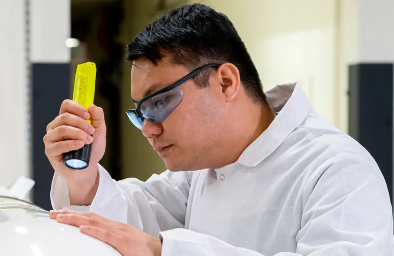 male engineer wearing safety goggles and a lab coat while inspecting a product with a flashlight