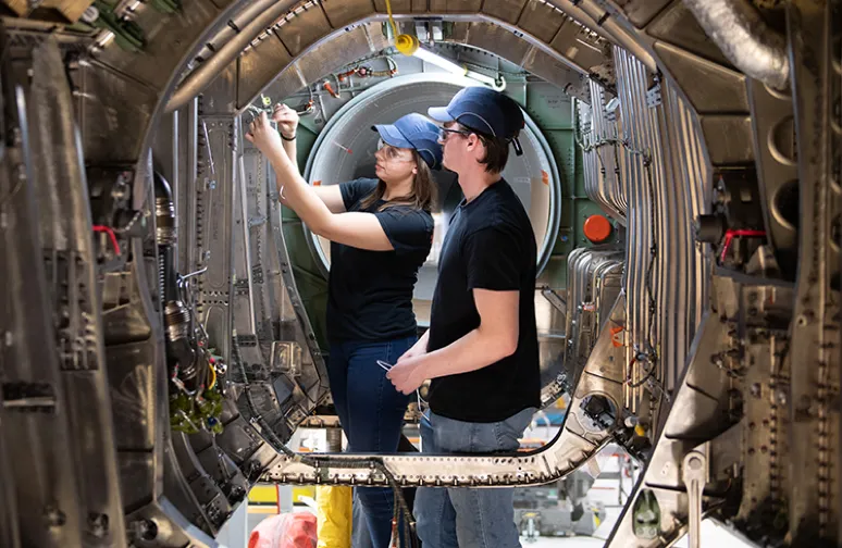 male and female engineer wearing safety goggles and working on the inner hull of an airplane