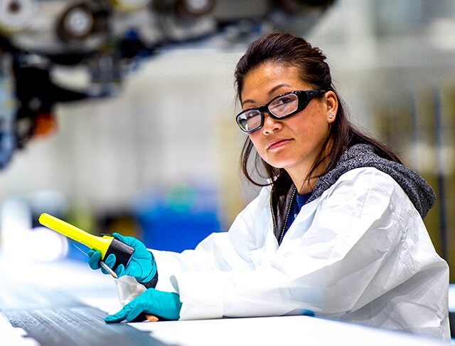 female employee wearing safety goggles and a lab coat in a manufacturing facility