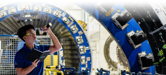 employee wearing a reflective vest and inspecting an aerospace engine