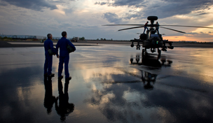 Two service members standing next an Apache helicopter