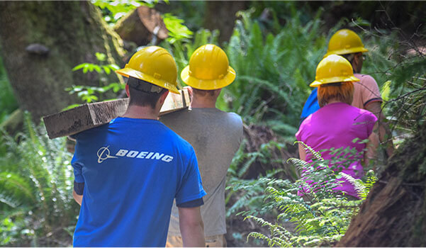 Men and women wearing hard-hats and walking in wooded area