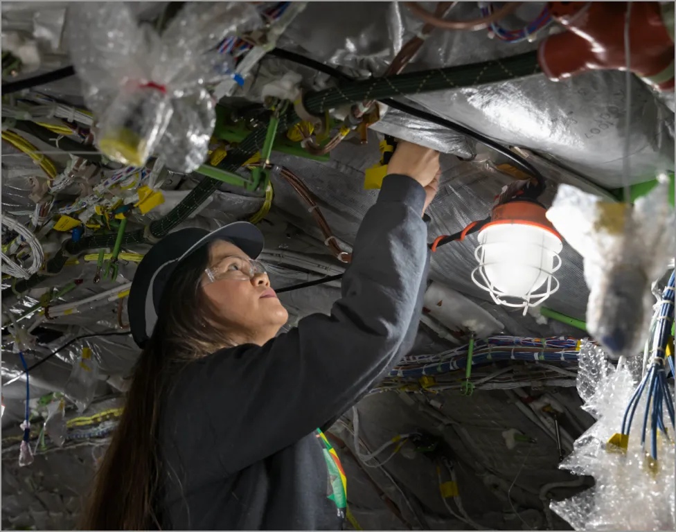 Technician wearing safety gear inspects a complex electrical panel with multiple colored wires and components