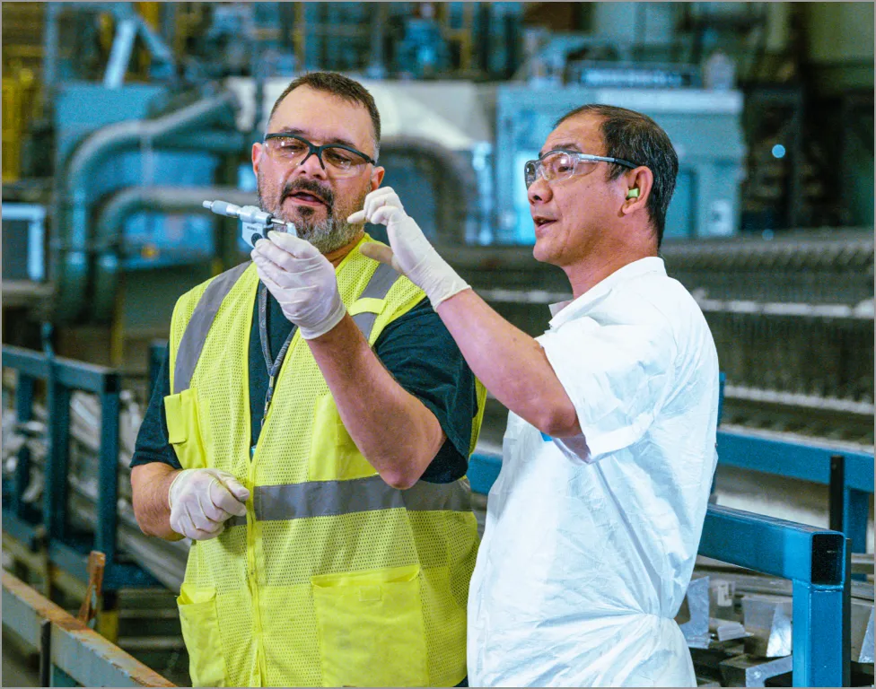 Two workers in a factory examining a machine part