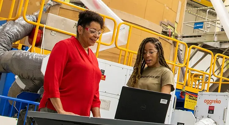 2 black female employees wearing safety goggles and looking at a laptop