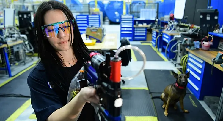 young female employee wearing safety goggles and handling a piece of machinery