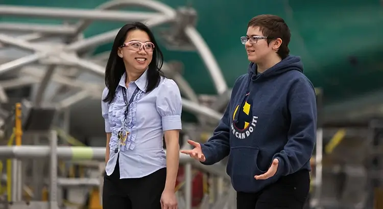 two engineers wearing safety goggles and chatting in front of a large aerospace project