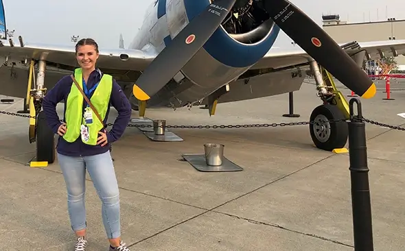 young female wearing a reflective vest and standing in front of a display airplane