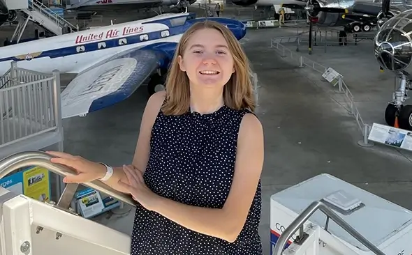 smiling young woman standing atop an airstair with airplanes on display in the background