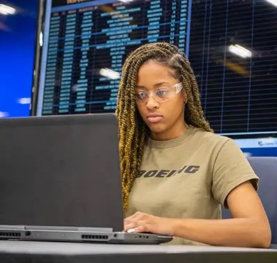 young black female programmer working on her laptop in front of a large panel of screens