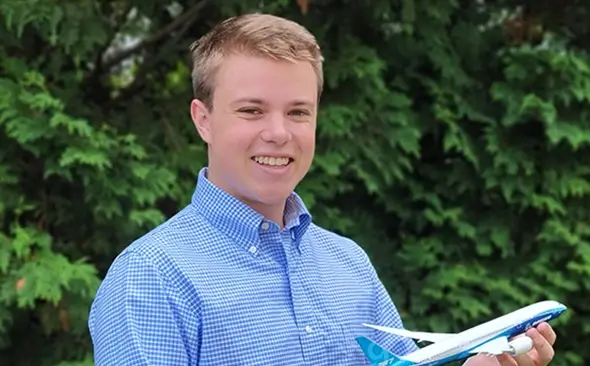 male youth wearing office attire and holding up a model of Boeing plane