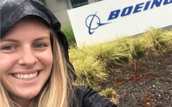 young female in a raincoat smiling in front a building with the Boeing logo in view
