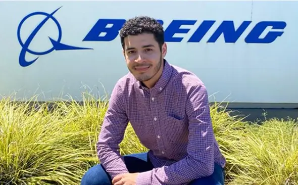 young male smiling in front of a building with the Boeing logo in view