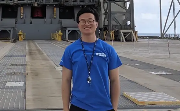young Asian male smiling as he stands on an aircraft carrier