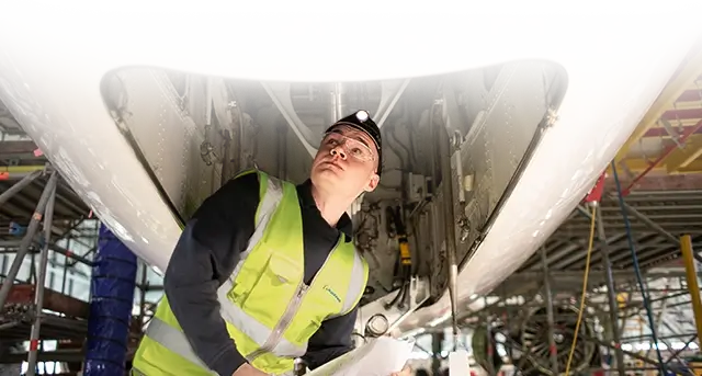 employee wearing a reflective vest and inspecting an aerospace engine