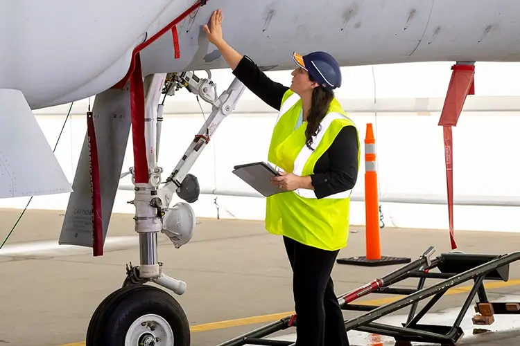 female employee wearing safety vest and inspecting the underside of an airplane