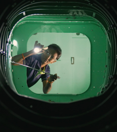 female employee wearing safety vest and inspecting the underside of an airplane