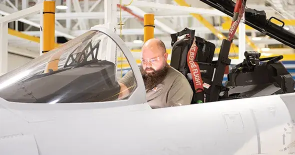 male employee sitting in a jet's cockpit and testing the control panel