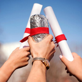 Raised hands clink diplomas and a Chipotle burrito in celebration of graduation