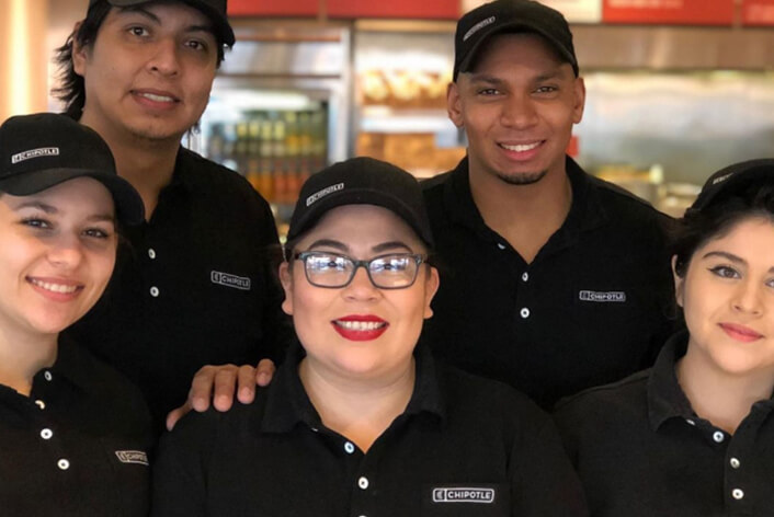 Chipotle Restaurant Crew y Manager posan felices para una foto grupal en el restaurante.