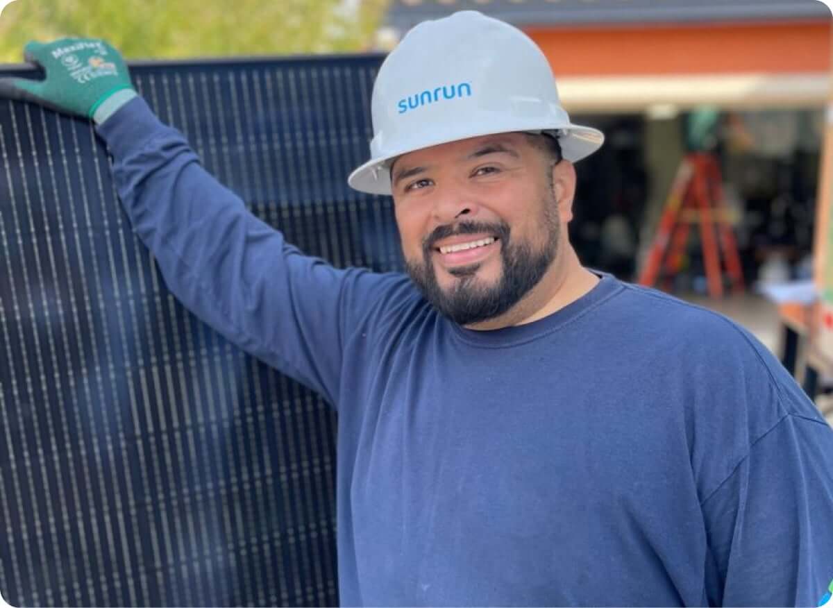Smiling man in hard hat stands next to a solar panel