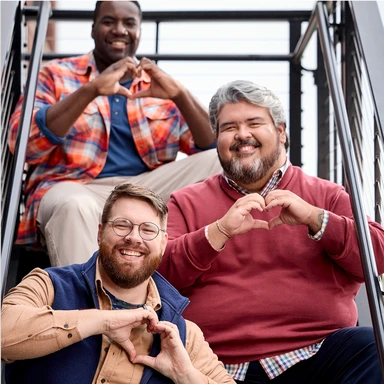 Three men standing together and smiling while forming a heart with their hands