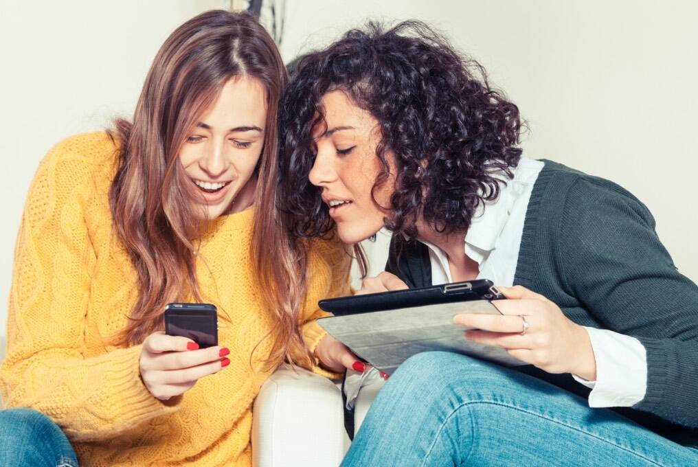 Twee vrouwen zitten en laten elkaar hun mobiele apparaten zien.