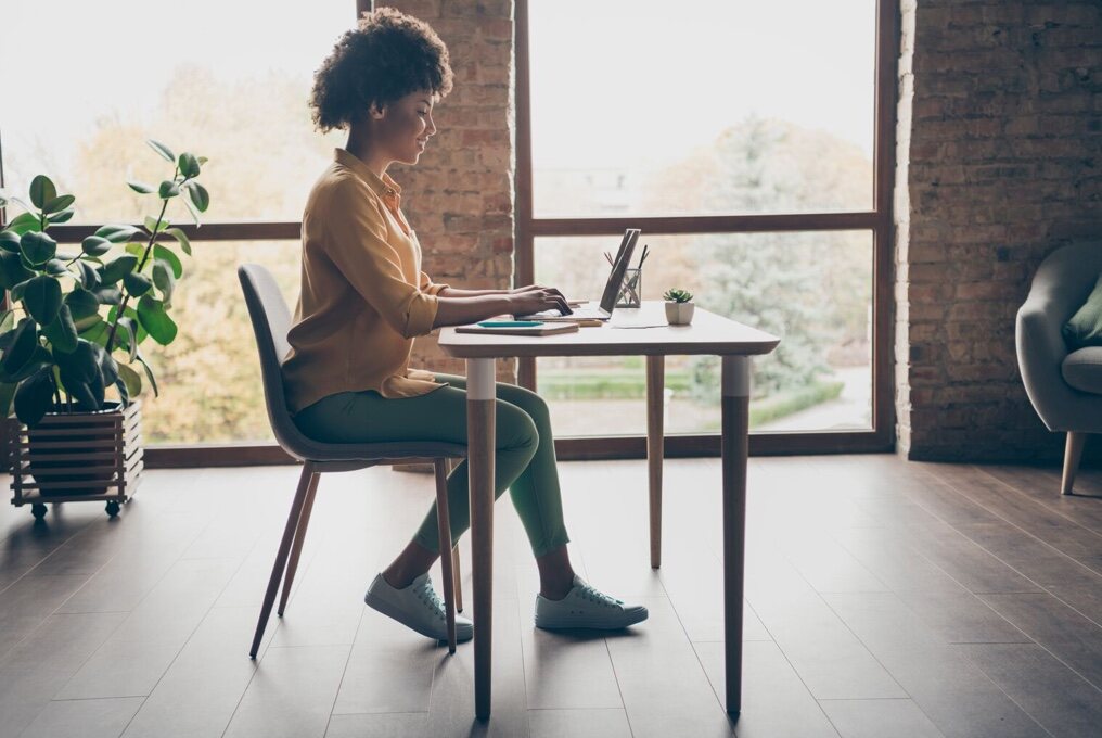 Uma mulher usa um laptop enquanto está sentada à mesa.