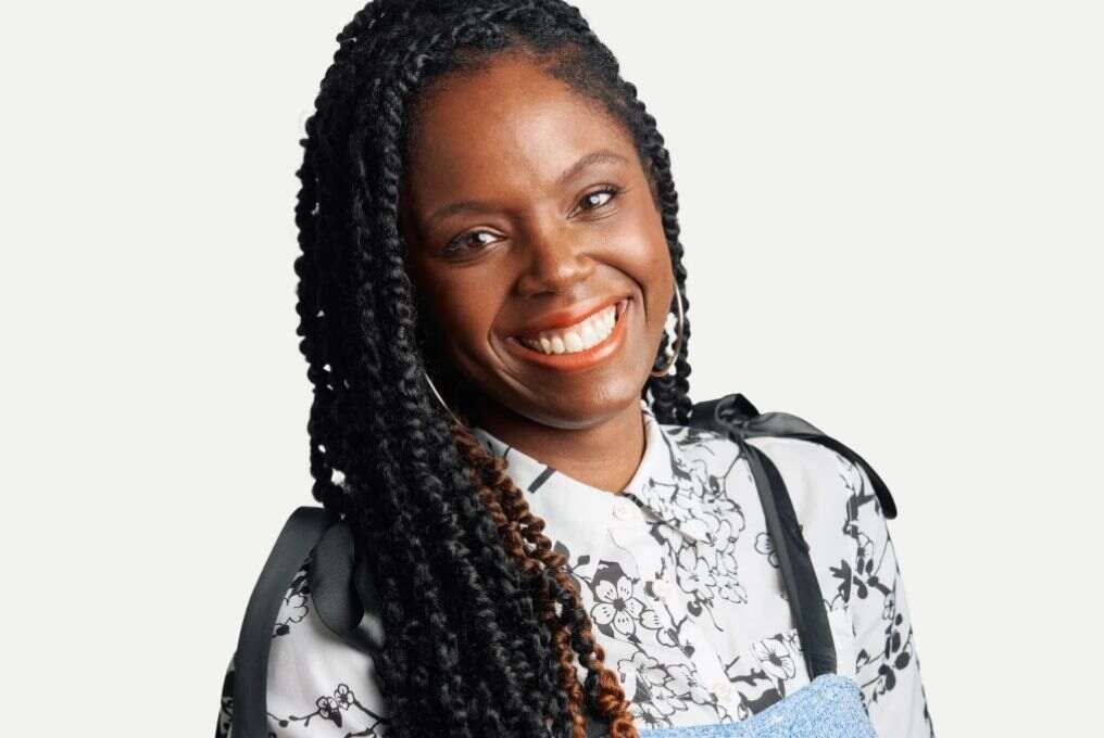 Smiling woman with long braids in floral shirt.