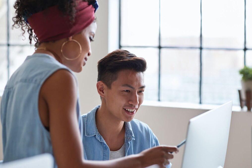 A man and woman sitting together, focused on a laptop screen.