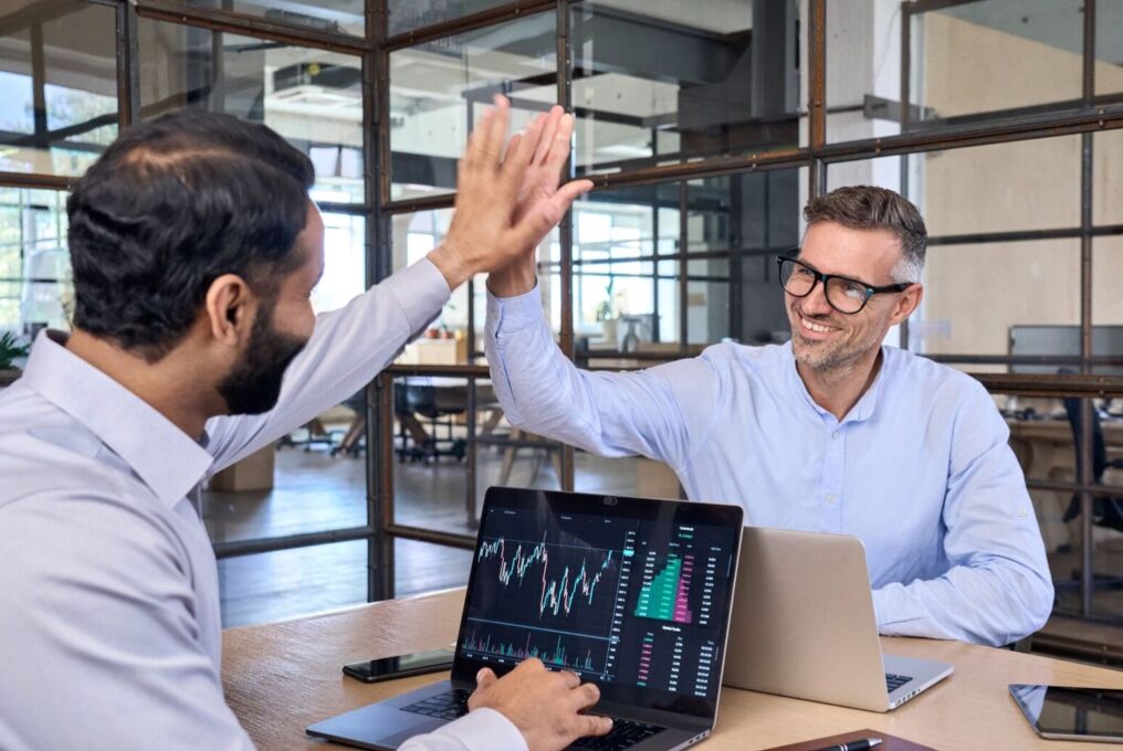 Dos hombres celebran el éxito con un high five en una mesa.