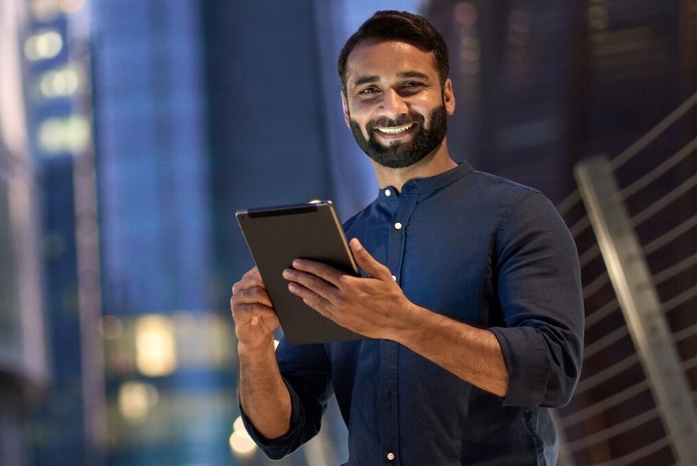 Een bebaarde man in een blauw shirt houdt een tablet vast.