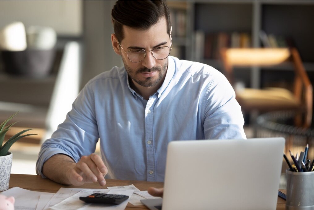 A man using a laptop at a wooden desk in a residential environment.