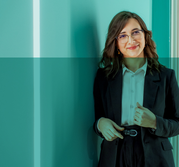 Professional woman in business suit and glasses standing in front of green wall.