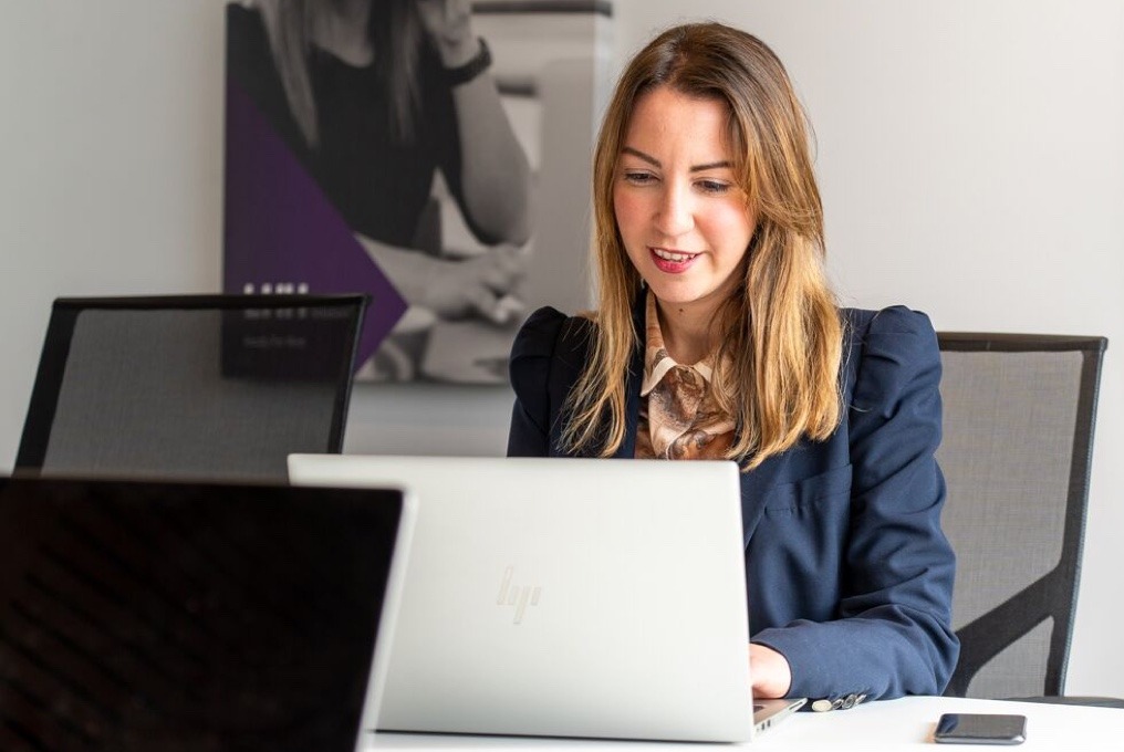 A woman in suit working on laptop at desk.