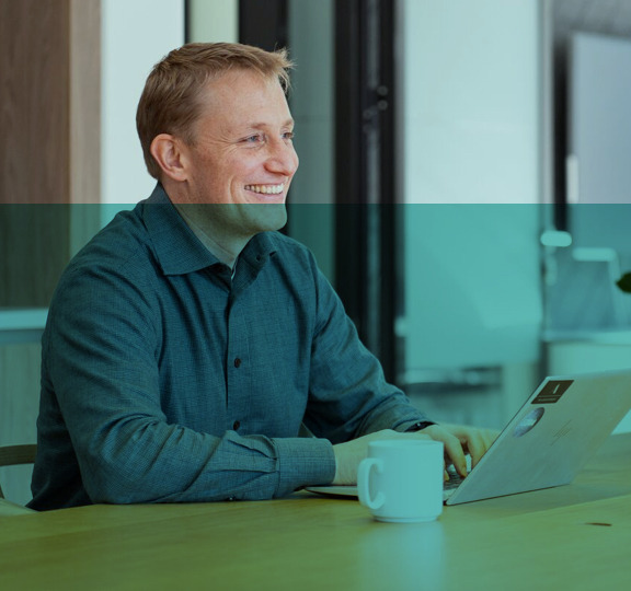 Glimlachende man die op een laptop werkt aan een bureau.