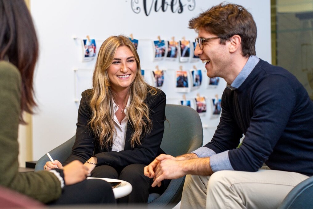 Drie personen bespreken iets in een vergaderruimte tijdens een bijeenkomst.