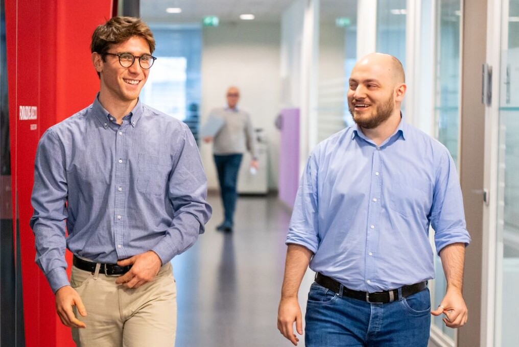 Two businessmen walking in a modern office hallway.