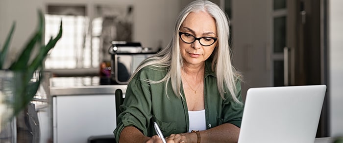 Lady writing at her desk in front of her laptop