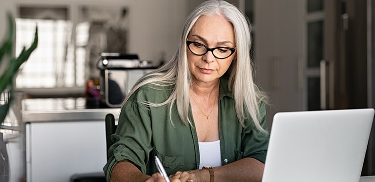 Lady writing at her desk in front of her laptop