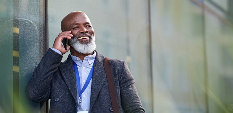 Man in a shirt and jacket talking on a mobile phone leaning against a glass wall